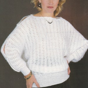 May include: White knitted sweater with a loose fit and openwork design. The sweater has a boat neck and long sleeves with button details.