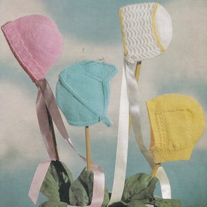 May include: Four knitted baby bonnets in pink, blue, white, and yellow with matching ribbon ties. The bonnets are displayed on sticks with green leaves.