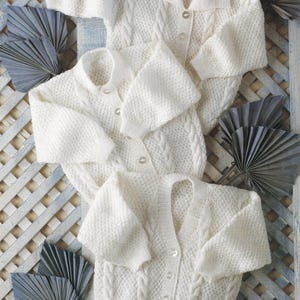 May include: Three white knitted baby cardigans with button fastenings and cable knit patterns.