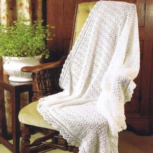 May include: A white crocheted blanket with a delicate lace border draped over a wooden chair with a green plant in a white pot on a side table.