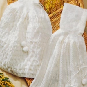 Pode incluir: Duas mantas de bebé de malha branca com um design de crochê e pompons. Uma manta tem capuz.