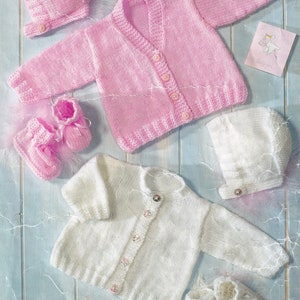 May include: Two knitted baby cardigans, one pink and one white, with matching hats and booties. The pink cardigan has buttons down the front and the white cardigan has pearl-like buttons. The booties are pink and white.