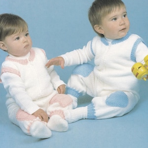 Op de afbeelding: Twee baby's dragen witte gebreide rompertjes met contrasterende knie-patches. Eén baby draagt roze knie-patches en de andere draagt blauwe knie-patches.