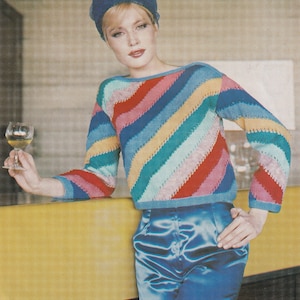 May include: A multi-coloured striped sweater with long sleeves, in shades of red, pink, blue, and green. The sweater is worn with high-waisted, satin blue trousers and a matching blue headband. The diagonal stripes give the sweater a retro appearance.