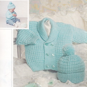 May include: A light blue knitted baby cardigan with a shawl collar and button closure, paired with a matching knitted hat with a pom-pom on top.