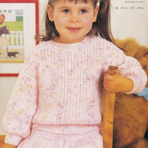 Può includere: Un maglione rosa chiaro a doppia maglia con macchie gialle e viola. Il maglione ha maniche lunghe e una trama a coste. Il testo "DOUBLE KNIT" e le misure "46-61cm. (18-24ins.)" sono visibili.