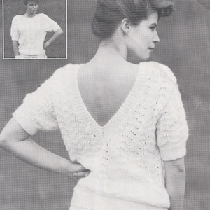 May include: A white knitted sweater with a deep V-neck and short sleeves. The sweater has a delicate openwork pattern.