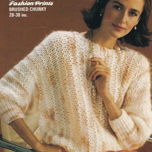 May include: A white and peach brushed chunky knit sweater with a round neckline. The sweater has a subtle striped pattern and is shown on a model wearing a pearl necklace.