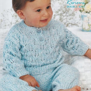 Puede incluir: Conjunto de bebé de punto azul claro, que incluye un suéter con tres botones y pantalones a juego. El conjunto tiene un delicado diseño calado. El texto "Riviera DOUBLE KNIT" es visible en la esquina superior derecha.