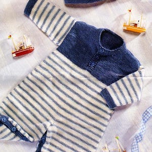 May include: A blue and white striped knitted baby onesie with a matching blue and white striped knitted hat. The onesie has a button closure at the neck and poppers at the crotch. The hat has a white tassel.