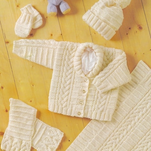May include: A white knitted baby set including a cardigan, hat, booties, and a blanket. The set features a cable knit pattern.