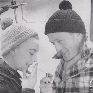 Può includere: Una fotografia in bianco e nero di due persone che indossano berretti di lana. La donna a sinistra indossa un berretto grigio chiaro con un pon pon bianco e fuma una sigaretta. L'uomo a destra indossa un berretto nero con un pon pon nero. Tiene un accendino in mano. La foto è tratta da una pubblicità vintage per P&B Wools.