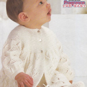 May include: A white knitted baby cardigan and matching leg warmers. The cardigan has a button closure and a delicate lace pattern. The text "Cotton & Fragrance For Baby" is printed on the background.