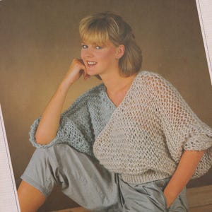 May include: A light blue and white knitted jumper with a loose fit and a V-neck. The jumper is made of a soft, airy yarn and has a delicate, openwork design.