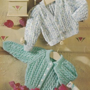 May include: Two long-sleeved knit cardigans with button-down fronts and textured cable patterns. The top cardigan is a variegated light blue and white, while the bottom cardigan is a solid mint green. Both feature ribbed cuffs and necklines.