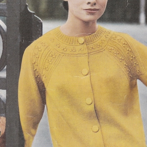 Puede incluir: Un cárdigan amarillo con botones y un diseño de punto. El cárdigan tiene un cuello redondo y mangas largas.