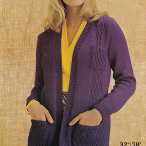 Pode incluir: Um casaco de malha roxo com um padrão de trança, com decote em V e dois bolsos de remendo. O casaco é aberto na frente e tem mangas compridas. O texto "32/38" e "D.K." está impresso no canto inferior direito da imagem.