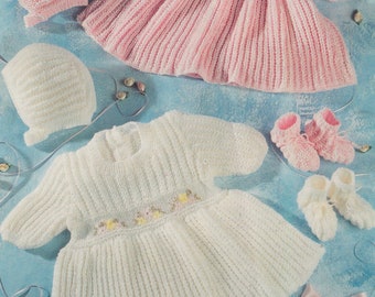 May include: Two knitted baby dresses, one white and one pink, with matching knitted hats and booties. The dresses have a scalloped hem and are decorated with embroidered flowers.