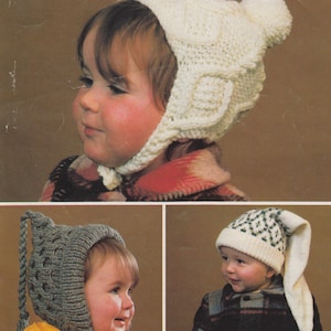 May include: Three children wearing different knitted hats with ear flaps. The hats are in white, grey, and white with green accents. The hats have long tails that hang down the back.