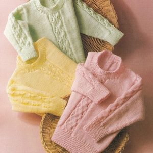 May include: Three knitted jumpers in different pastel colours: light green, yellow, and pink. Each jumper has a cable knit pattern and a round neckline.