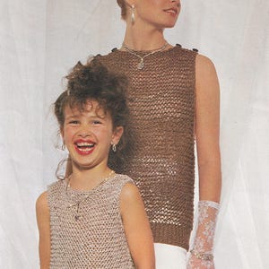 Puede incluir: Dos tops sin mangas en un diseño de tejido abierto marrón claro y beige. La mujer lleva un top marrón con collar y pendientes. La niña lleva un top beige con collar y pendientes. Ambas llevan guantes de encaje.