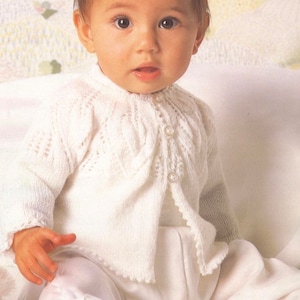 Peut inclure: Un cardigan blanc en tricot pour bébé avec une fermeture boutonnée et un motif de dentelle délicat.