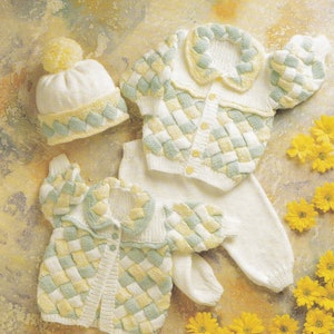 May include: A knitted baby outfit set in white with green and yellow accents. The set includes a hat, cardigan, and pants. The cardigan has a braided collar and button closure.