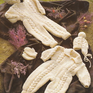 Könnte beinhalten: Zwei gestrickte Baby-Outfits in Weiß mit Zopfmuster. Ein Outfit beinhaltet eine passende Mütze und Fäustlinge. Die Outfits liegen auf einem braunen Stoffhintergrund.