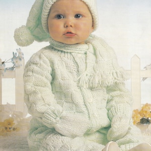 May include: A light green knitted baby outfit with a matching hat, mittens, and scarf. The outfit features a cable knit pattern and a button closure. The hat has a pom-pom on top. "DOUBLE KNIT" and "16" TO 22" are printed on the image.