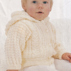 Op de afbeelding: Een wit gebreid babyvest met een capuchon en knoopsluiting. Het vest heeft een kabelbreipatroon en is gemaakt van zacht garen.