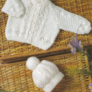 Puede incluir: Conjunto de bebé de punto blanco que incluye una rebeca con botones y un gorro a juego con pompón. El conjunto está hecho de un hilo suave y texturizado. La rebeca tiene un delicado diseño calado.