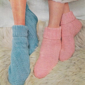 May include: A pair of knitted socks, one blue and one pink, with a cable knit pattern. The socks are on a white fluffy surface.