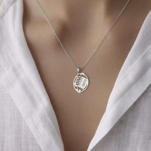 May include: A silver necklace with a football pendant. The pendant is cut out in the shape of a football with the word 'JACK' inscribed inside.