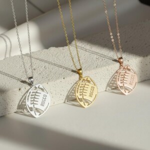 May include: Three silver necklaces with football shaped pendants. The pendants have the names 'Skylar', 'Carter', and 'Hayden' engraved on them.