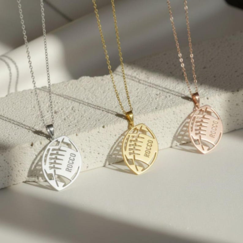 May include: Three silver necklaces with football shaped pendants. The pendants have the names 'Skylar', 'Carter', and 'Hayden' engraved on them.