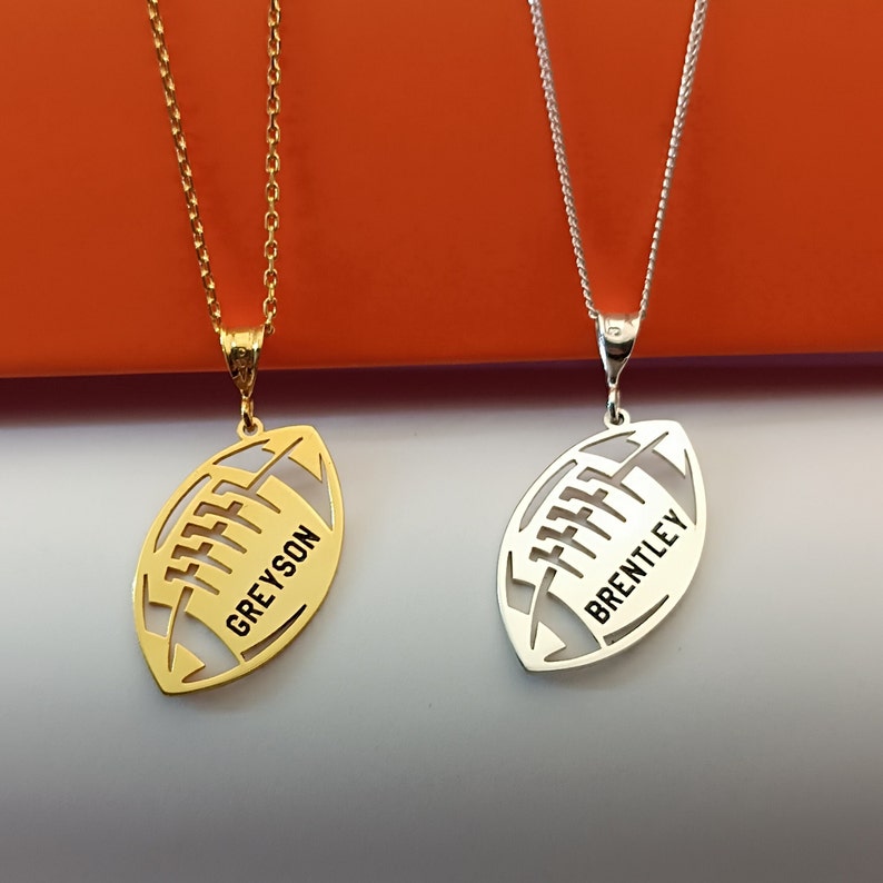 May include: Two silver necklaces with football-shaped pendants. The pendant on the left necklace says "Greyson" and the pendant on the right necklace says "Brentley".