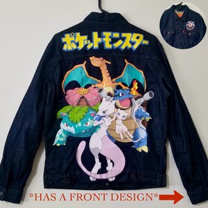 May include: A dark blue denim jacket with a colorful Pokemon design on the back. The design features the text "ポケットモンスター" in Japanese, and includes characters like Venusaur, Charizard, Blastoise, and Mewtwo.