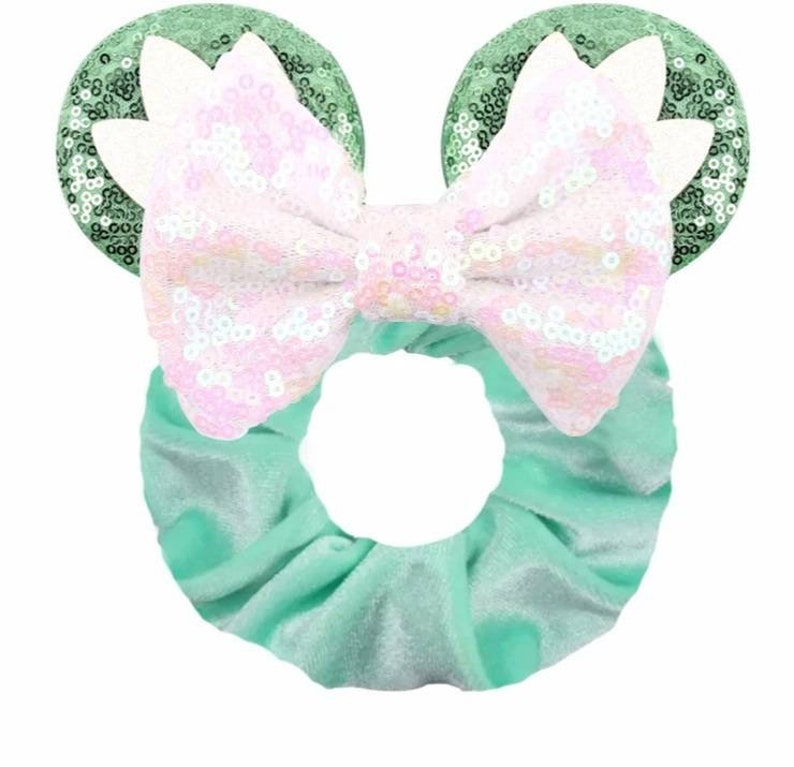 May include: A green velvet scrunchie with a large pink and white sequined bow and green sequined mouse ears.