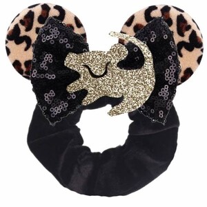 May include: Black velvet hair scrunchie with a black and gold sequined bow and leopard print fabric ears. The bow features a gold glitter lion silhouette.