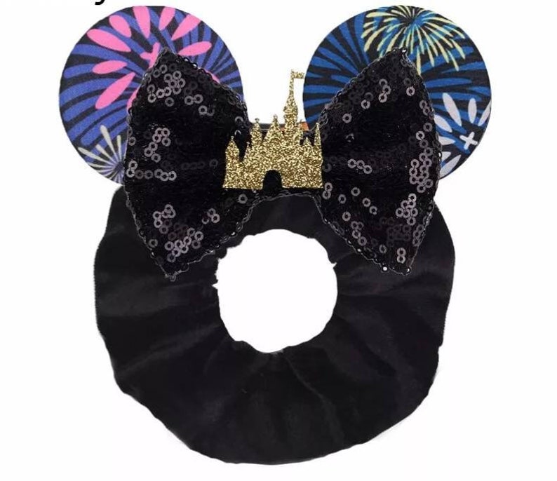 May include: Black sequin bow with a gold glitter castle charm, attached to a black velvet headband with blue and pink firework print ears.