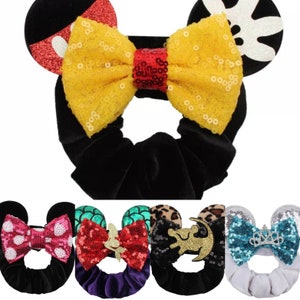 May include: A set of five hair scrunchies with different character-themed ears and bows. The scrunchies are made of black velvet and have a variety of colors and patterns, including red, yellow, blue, green, and pink.