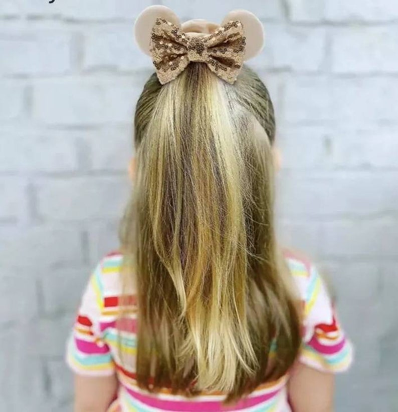 May include: A gold glitter bow with mouse ears, attached to a ponytail.