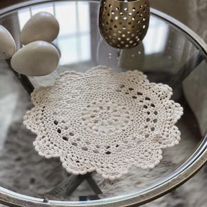 Peut inclure: Un napperon en crochet beige avec un motif floral délicat, placé sur une table en verre.