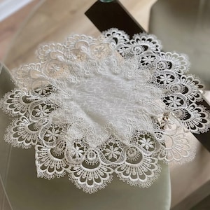 May include: Several white lace doilies with detailed floral and scalloped edges. The doilies are placed on a pale green surface, highlighting their delicate patterns and textures. The lace appears to be made of a fine, soft material.