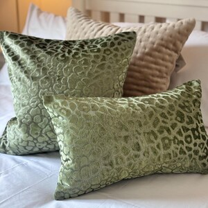 May include: Two square and rectangular throw pillows featuring a raised, textured olive green velvet leopard print pattern, accompanied by a single beige quilted throw pillow, all arranged together on a white surface.