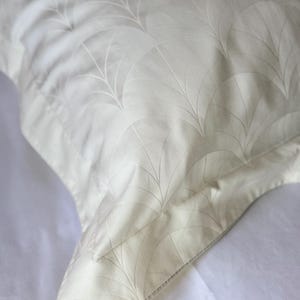 May include: A white pillowcase featuring a subtle, tonal fan-shaped pattern across the fabric. The pillowcase has a wide, stitched border along the edge, creating a defined frame for the repeating geometric design visible on the surface.