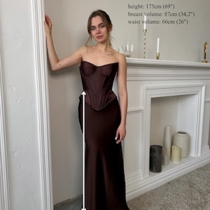 Peut inclure: Ensemble corset et jupe longue marron fonc&eacute;. Le corset est sans bretelles et structur&eacute;. La jupe longue mesure 100 cm de long. La mod&egrave;le mesure 175 cm de haut, avec un tour de poitrine de 87 cm et un tour de taille de 66 cm.