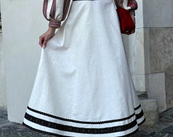 May include: A white skirt with a black lace trim and a red and black striped top. The skirt is long and flowing, and the top is fitted. The woman is wearing white sandals.