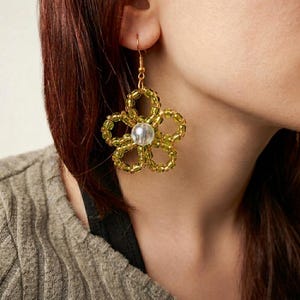 May include: A gold-coloured beaded flower earring with a clear, round bead in the centre. The flower has five petals and is made of small, round beads. The earring is worn on the ear.