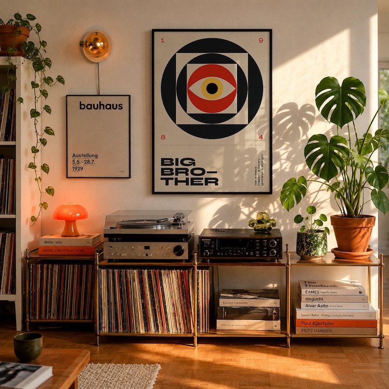 May include: A room with a mid-century modern aesthetic. A framed "Big Brother" poster hangs above a stereo system and vinyl record storage. A "Bauhaus" poster is also displayed. An orange mushroom lamp sits on a stack of books. A large potted plant is on the right.